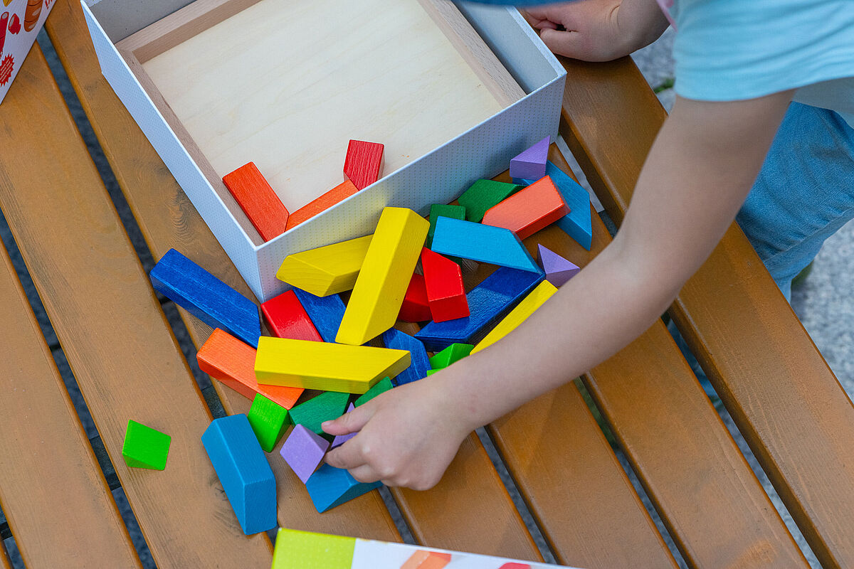 Symbolbild Spielen Eine Kinderhand greift nach ausgekippten bunten Holzklötzchen.
