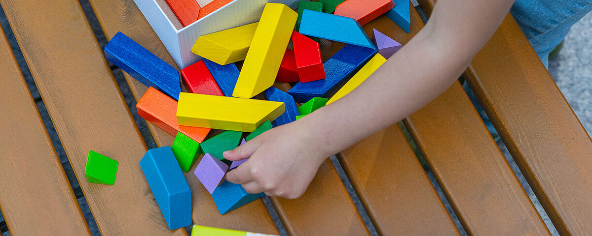 Symbolbild Spielen Eine Kinderhand greift nach ausgekippten bunten Holzklötzchen.