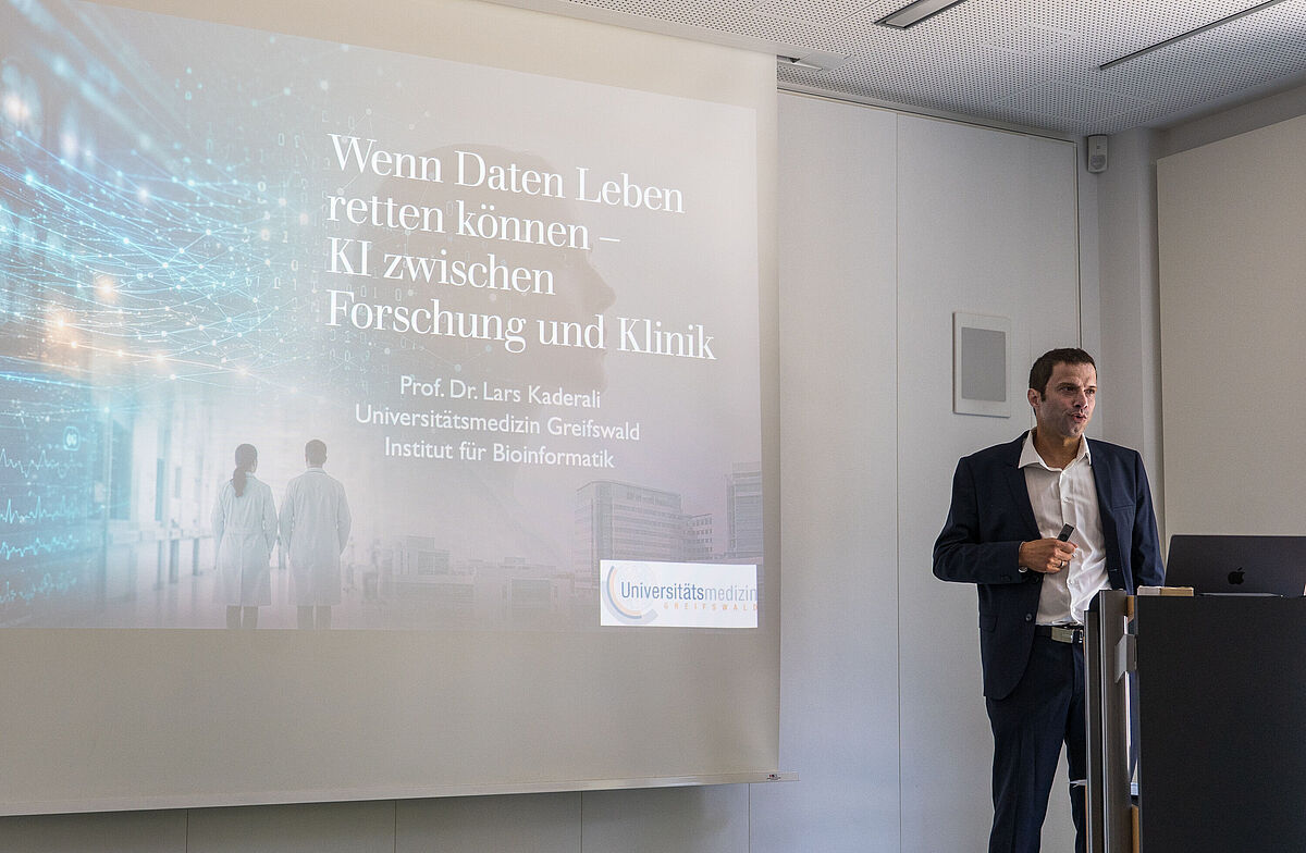 Ein Mann hält einen Vortrag vor einem großen Bildschirm mit Text zu KI und Forschung