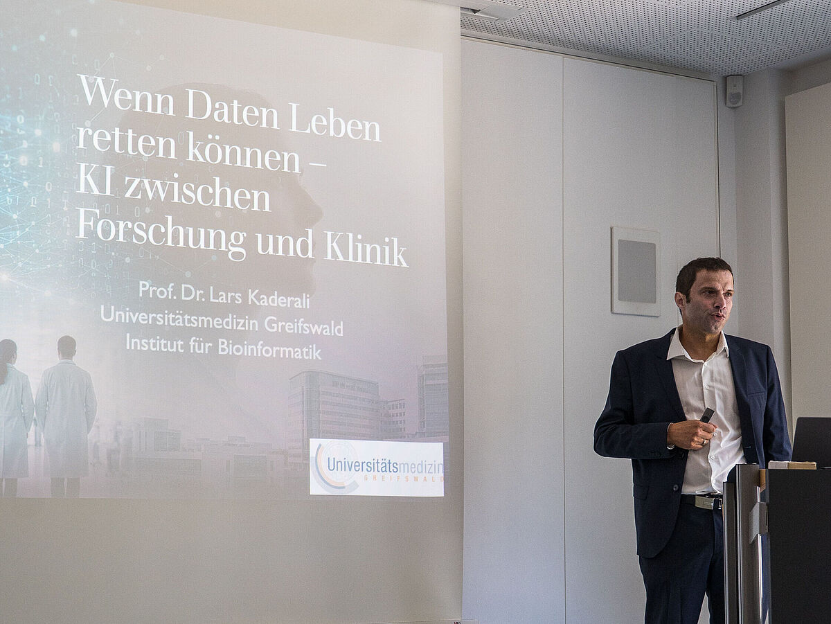 Ein Mann hält einen Vortrag vor einem großen Bildschirm mit Text zu KI und Forschung