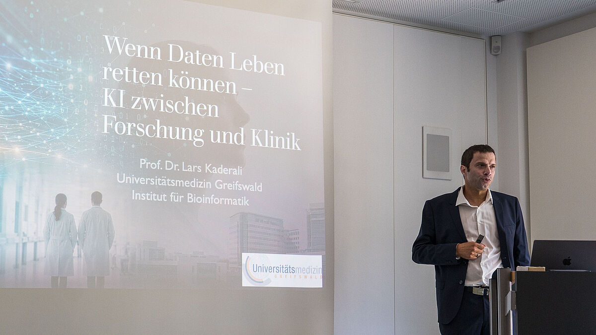 Ein Mann hält einen Vortrag vor einem großen Bildschirm mit Text zu KI und Forschung
