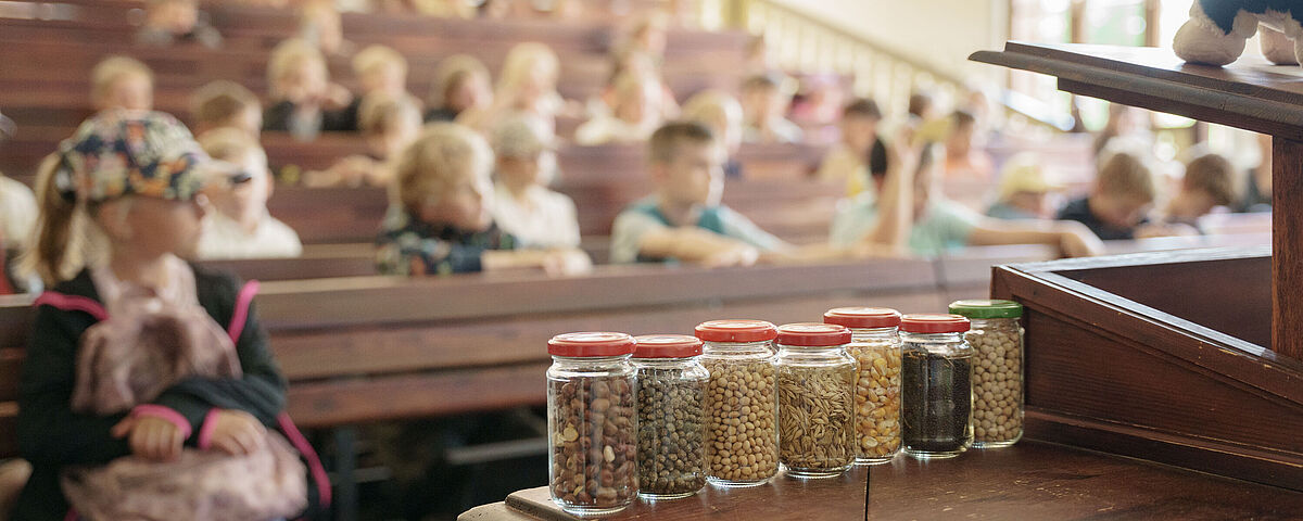 Kinder- und JugendUNI 2026 Kinder und Gläser gefüllt mit Materialien für einen Votrag in einem alten Hörsaal.