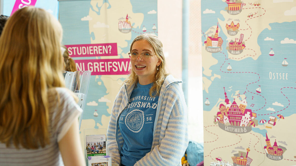 Eine junge Frau unterhält sich mit Menschen und berät sie freundlich zum Studium.