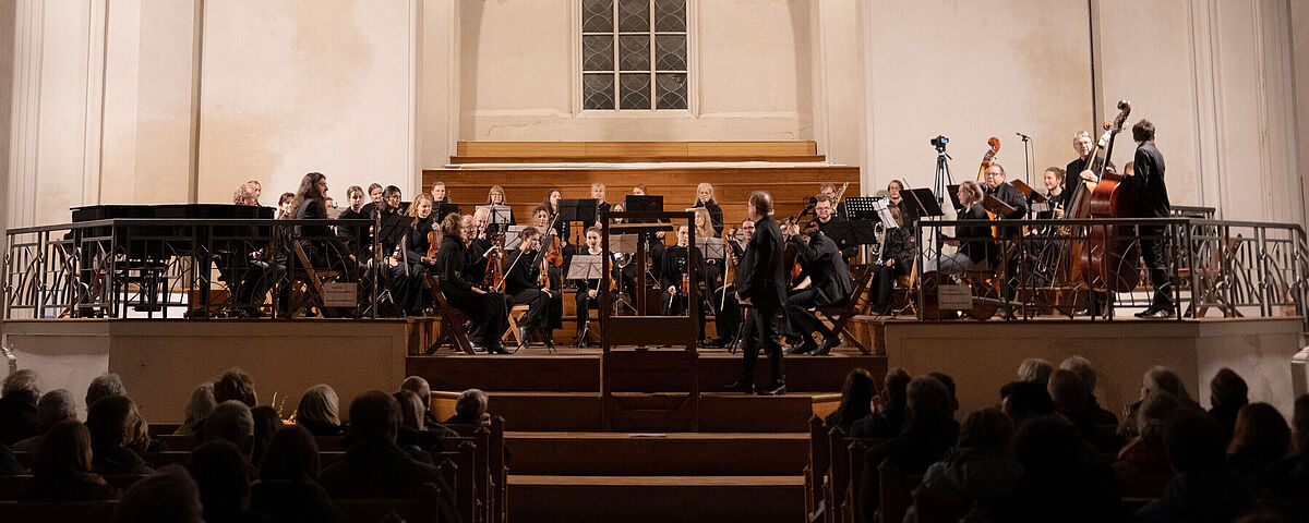 Vor dem großen sakralen Fenster des Doms sitzt das festlich gekleidete Universitätsensemble bereit für den Auftritt.