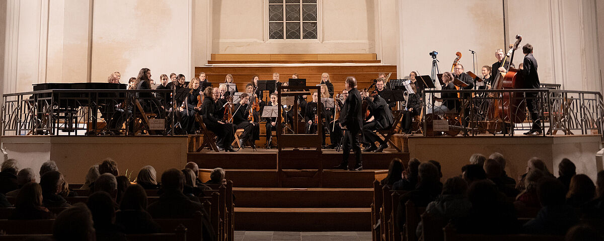 Vor dem großen sakralen Fenster des Doms sitzt das festlich gekleidete Universitätsensemble bereit für den Auftritt.