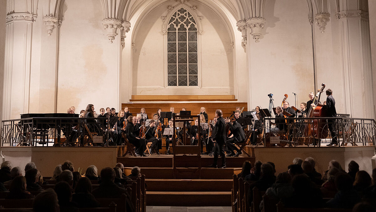 Vor dem großen sakralen Fenster des Doms sitzt das festlich gekleidete Universitätsensemble bereit für den Auftritt.