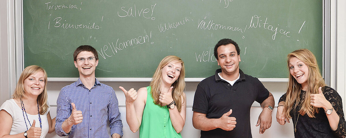 Several participants of a language course with thumbs up in front of a black board