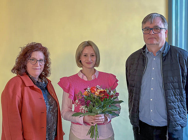 Drei Personen stehen in einer Reihe, die in der Mitte hält einen Blumenstrauß