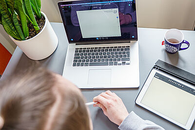 Eine Person sitzt vor einem geöffneten Laptop in einem Online-Meeting.