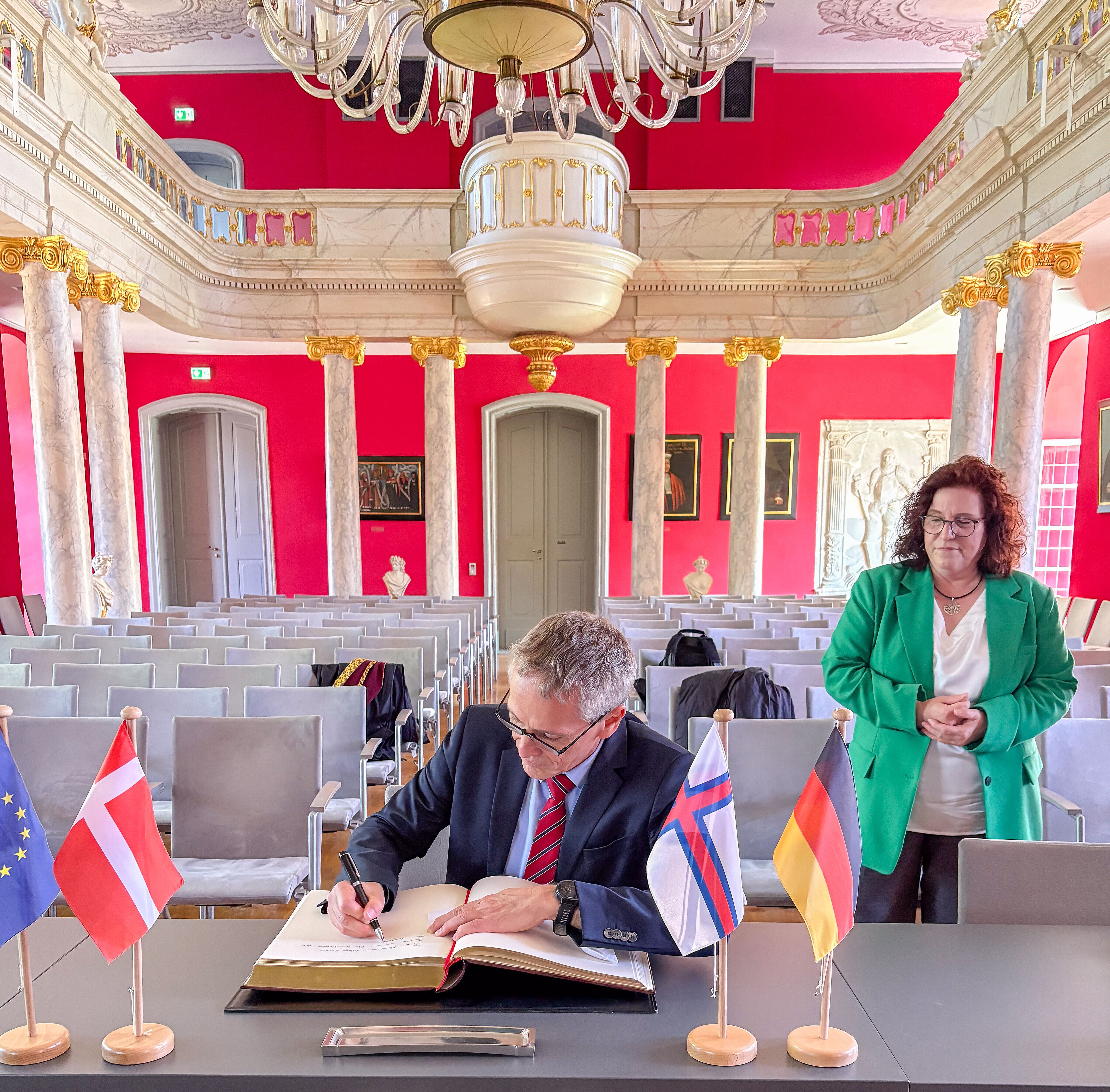 Besuch Dänische Delegation Besuch der dänischen Delegation während des 35. Nordischen Klangs: Der dänische Botschafter trägt sich in der Aula der Universität in das Goldene Buch ein. Schräg hinter ihm steht die Rektorin.