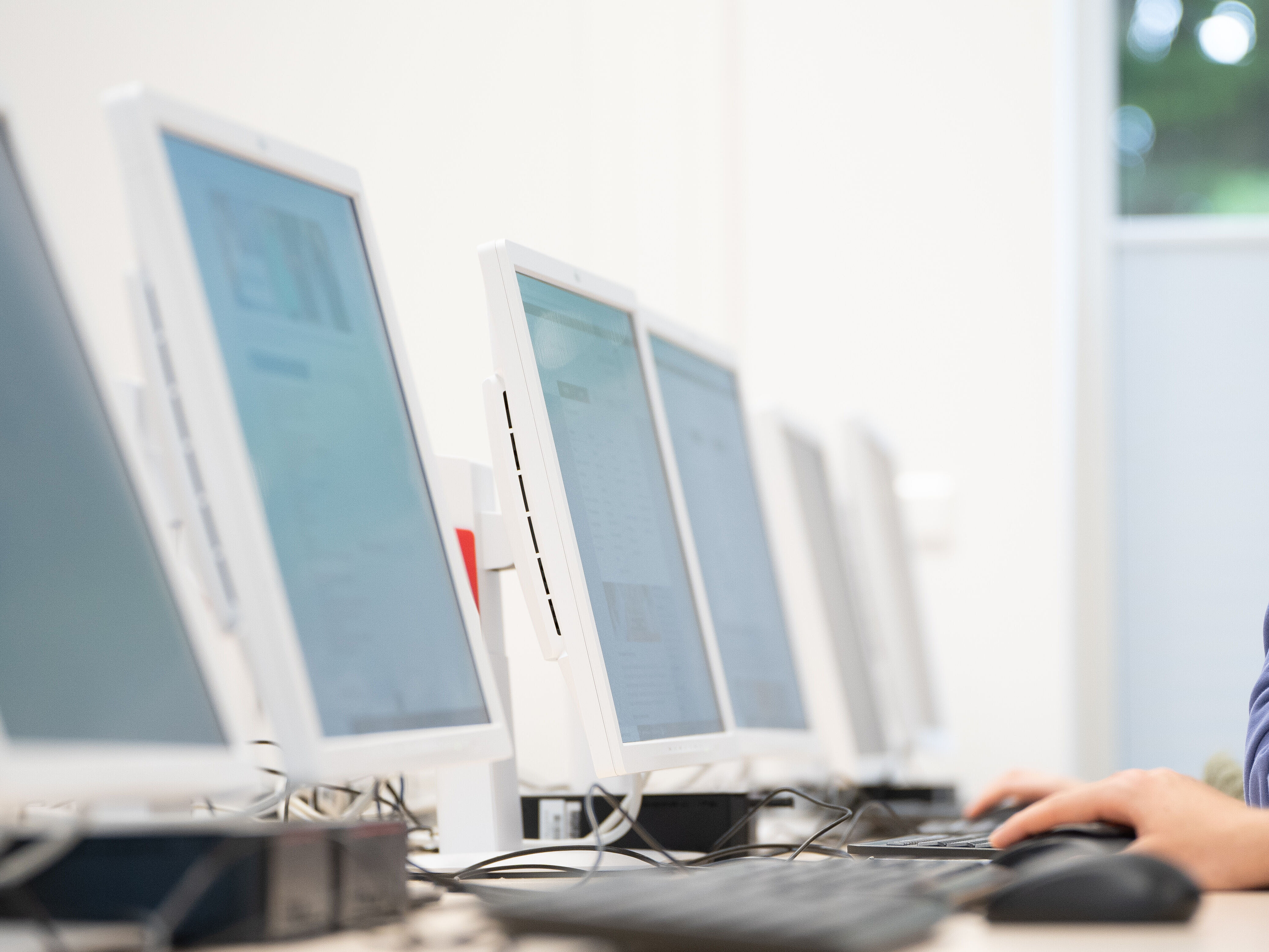 Studierende im Rechenzentrum Das Bild zeigt mehrere Comuterbildschirme. Am rechten Rand ist eine Studentin zu sehen, die an einem Computer arbeitet.