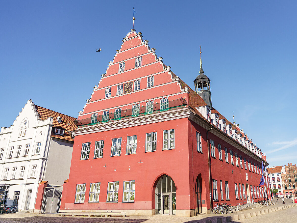Das rote Rathaus der Universität Greifswald vor einem strahlend blauen Himmel.