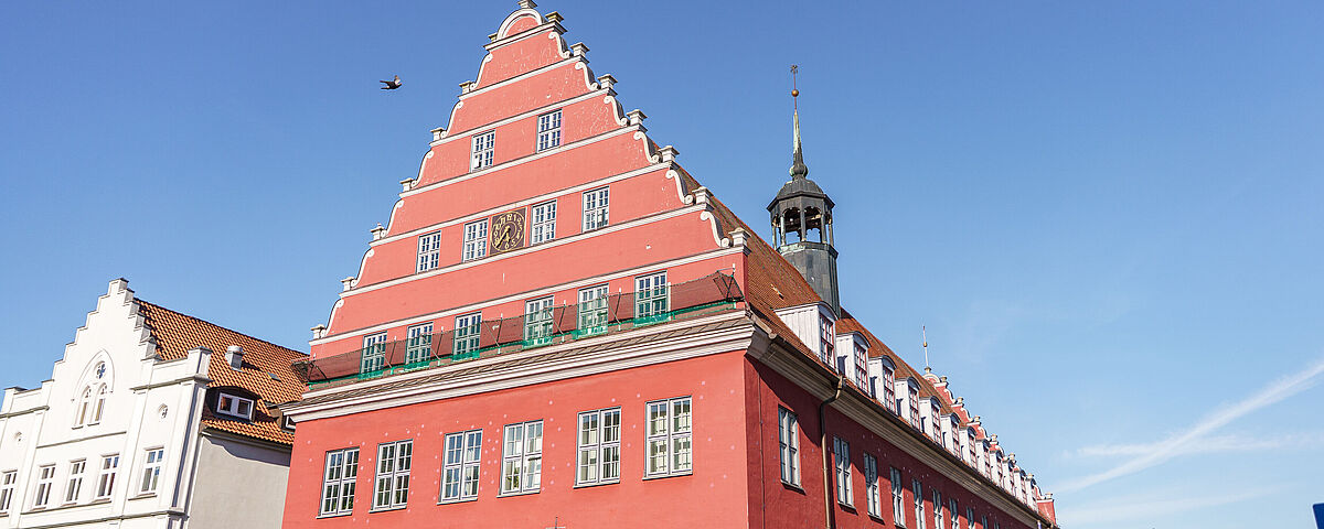 Das rote Rathaus der Universität Greifswald vor einem strahlend blauen Himmel.